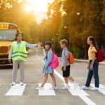 Road Traffic Safety. School Bus Assistant Helping Kids Cross Road By Crosswalk